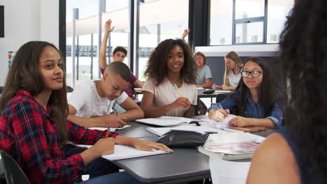 high school kids raise hands, teacher sitting at their desk