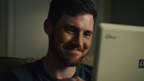 a moment of joy and connection as a young man smiles while looking at his laptop screen, capturing the essence of digital communication and personal interaction.