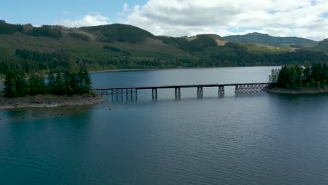 aerial establishing shot over campbell river upper lake trestle bridge on a partially cloudy day in spring near strathcona regional park in vancouver island, british columbia, canada