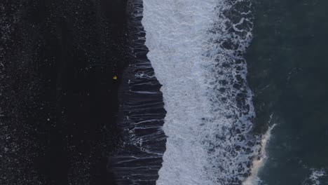 top view of man running away for waves at black sand beach, aerial