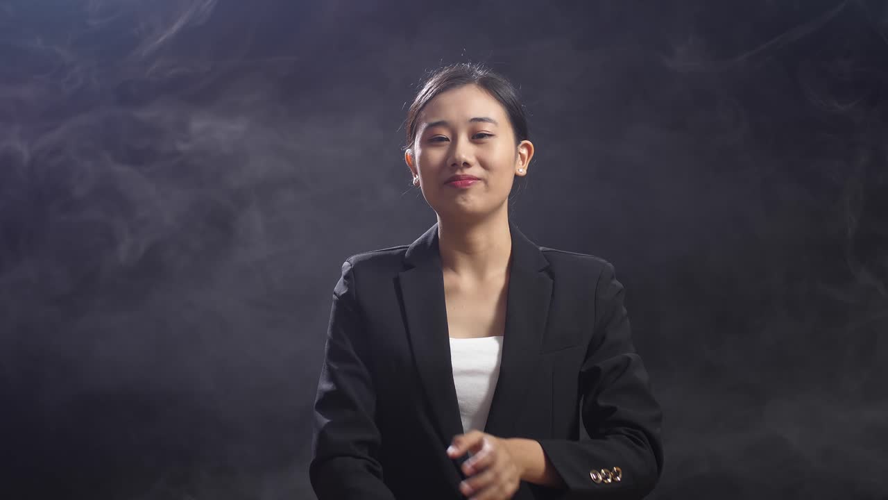 una mujer sonriente de habla asiática en traje de negocios cruzando los brazos mientras está de pie en el estudio de pantalla negra