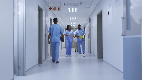 médico afro-americano e médica em discussão caminhando no corredor movimentado do hospital