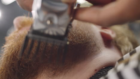 barber using hair clippers of beard of client