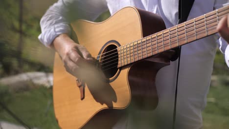 Mann,-Der-Saiten-Auf-Der-Gitarre-Zupft,-Detailaufnahme-Durch-Olivenbaumblätter,-Bokeh-Zeitlupe