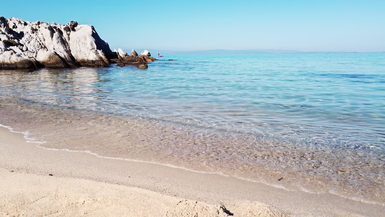 Ege Denizi kıyısı, plaj, suyun üzerindeki kayalar ve uzaktaki kara, Yunanistan. Ağır çekim