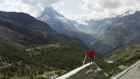 Aerial-passes-a-young-hiker-with-an-epic-view-over-the-Matterhorn,-Zermatt,-Switzerland