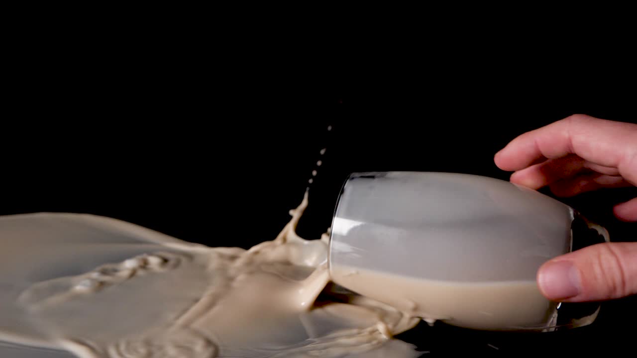 рука тянется к стакану с ореховым молоком и опрокидывает его, проливая жидкость на стол