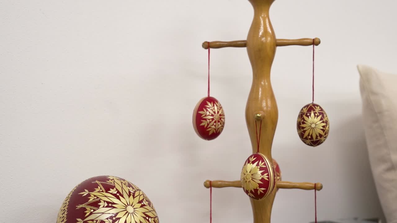 Hanging traditional Hungarian Easter eggs with red and gold patterns on a wooden stand