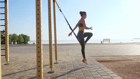 entrenamiento al aire libre. correas de suspensión. entrenamiento con correas. mujer joven atlética está haciendo ejercicios de resistencia de todo el cuerpo usando cuerdas en bucle trx, en la playa durante la puesta o el amanecer. entrenamiento de fitness al aire abierto. concepto de estilo de vida saludable. deporte matutino