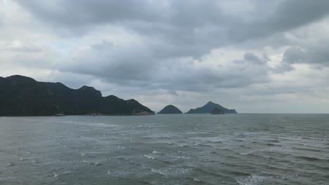 해안, 산, 수평선에 있는 섬, 아름다운 회색 구름으로 밀려드는 파도의 꾸준한 공중 영상