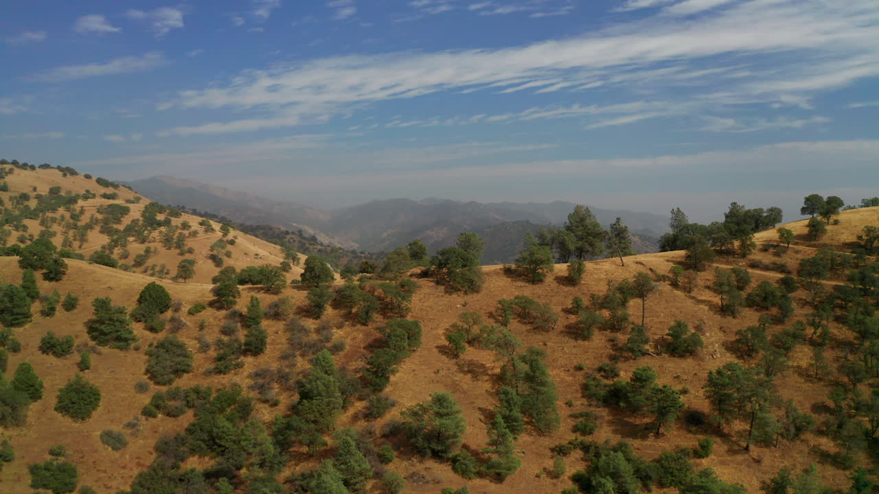 Vista aerea: discesa sotto una collina con la catena montuosa Rossa avvolta dal fumo in lontananza.