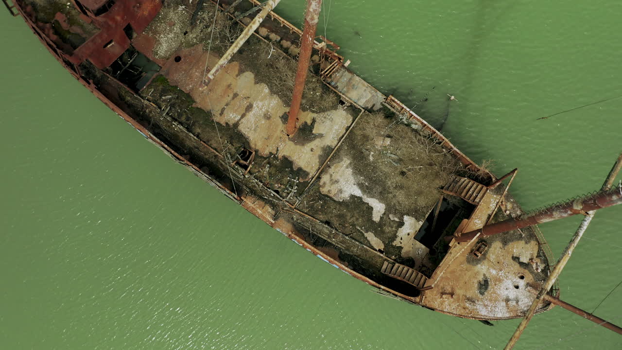 Rusty red shipwreck stuck in shallow green water
