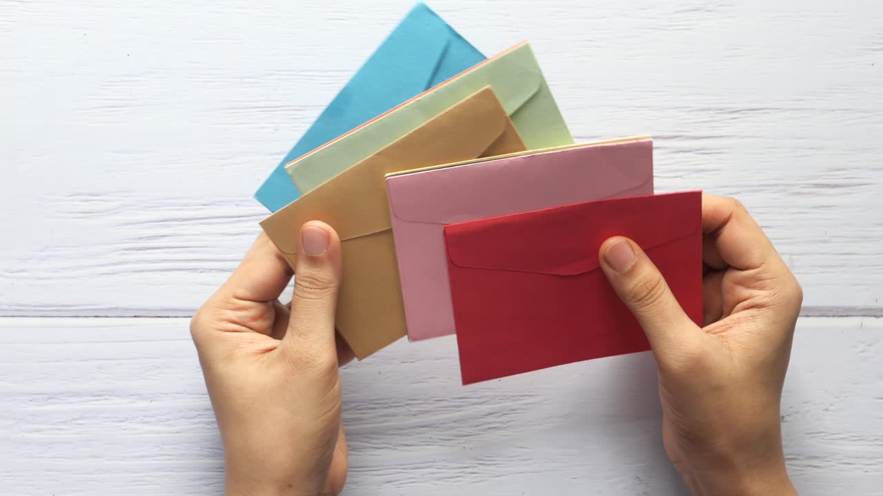 가운 나무 테이블 에 다채로운 봉투 와 카드 를 들고 있는 손 들