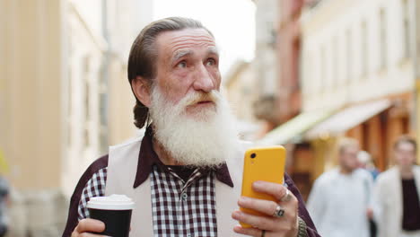 senior man walking on the street with a coffee and checking his phone