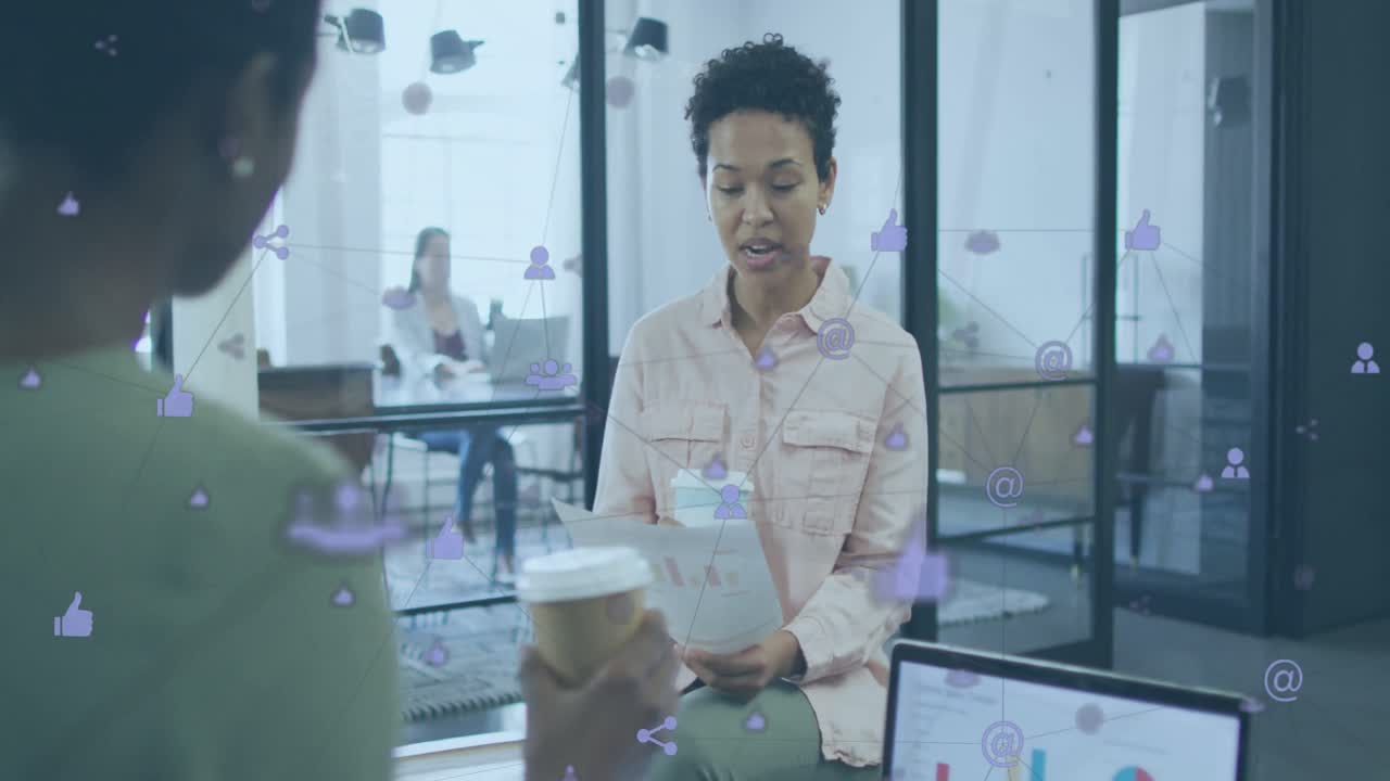 Animation of connected icons over diverse female coworkers discussing reports while drinking coffee