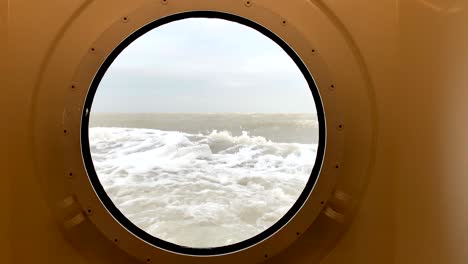 view through a porthole on a stormy sea with waves hitting the ship