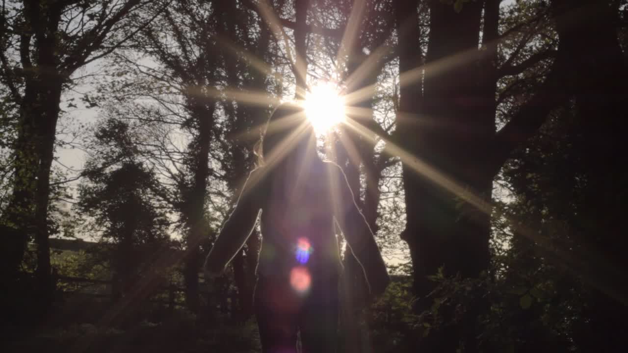Woman relaxing in woodland with lens flare at sunset wide shot