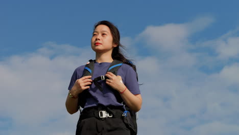 Retrato-De-Una-Joven-Modelo-Mochilera-Asiática-En-Cámara-Lenta-Durante-Un-Viaje-De-Viajero-Solitario-Llevando-Mochila-Contra-El-Cielo-Azul