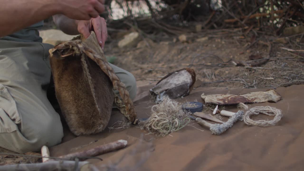 hombre caucásico de supervivencia desempaquetando brasa de una bolsa de cuero para preparar fuego en el campamento en el desierto