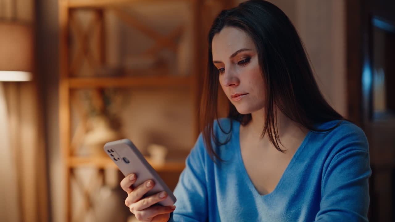 Primer plano de una morena triste mirando el móvil en el salón al atardecer. Mujer seria