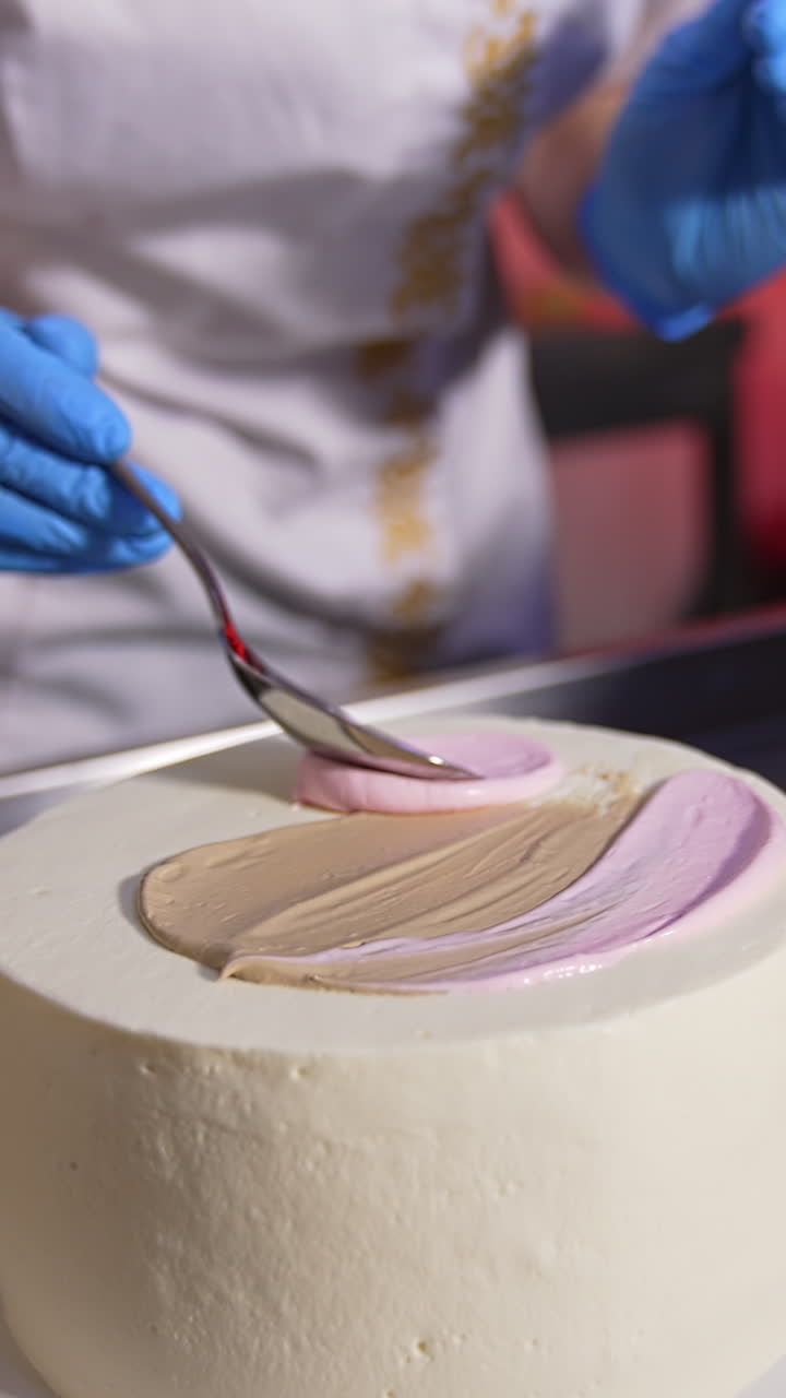 Pastry cook applies white cream with a spoon on top of the white cake. Close up. Chocolate cake at the table at backdrop. Vertical video