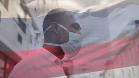 animation of flag of russia waving over african american man wearing face mask in city street