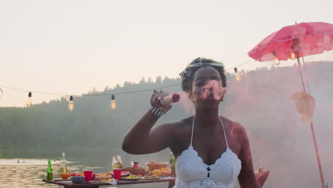 happy black woman dancing with colored smoke bomb at summer party