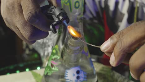una mano de hombre negro usando una antorcha para encender una mecha en preparación para fumar un bong de agua lleno de marihuana