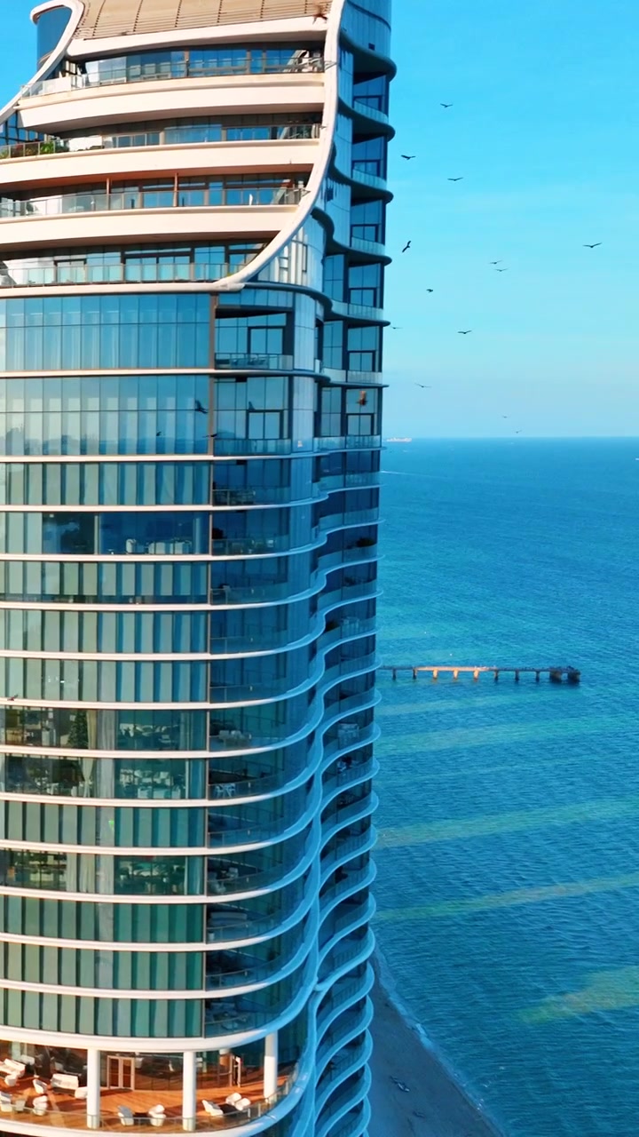 Longa costa com píer e torre em Sunny Isles Beach, Miami. Vista elevada de drone capturando resort alto à beira-mar, costa arenosa, vasto cais de madeira e mar turquesa. Vídeo vertical