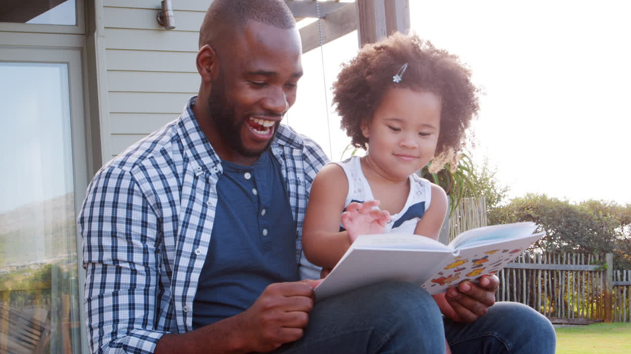 Padre di Colore e Giovane Figlia che Leggono un Libro all'Aperto.