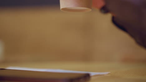 soft focus close-up of smartphone lying on napkin over wooden table, partial view of arm in background wearing long-sleeve shirt, creating subtle moment of stillness, casual indoor atmosphere, and modern lifestyle