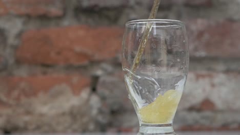 Toma-En-Cámara-Lenta-De-Verter-Cerveza-Fresca-En-Un-Vaso,-Fondo-De-Pared-De-Ladrillo-Naranja