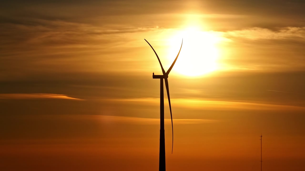 Einsame Windkraftanlage als Silhouette vor einem glühenden goldenen Sonnenuntergang, der den bewölkten Himmel beleuchtet. Drohnenaufnahme