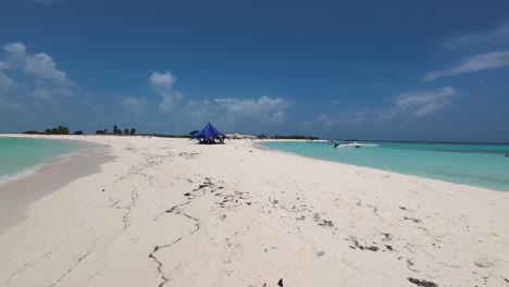 Paradise-white-sand-with-beach-tent-and-boat,-Los-Roques-background-pan-right