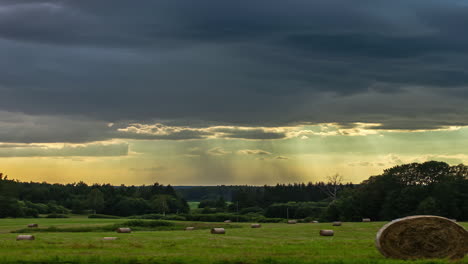 moody clouds over farm landscape with bales, rainfall in distance