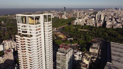 aerial orbit shot of residential block tower in suburb area of buenos aires - skyline in background during sunny day