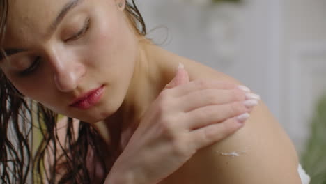 woman applying cream on her skin in bathroom while siting on bath tub