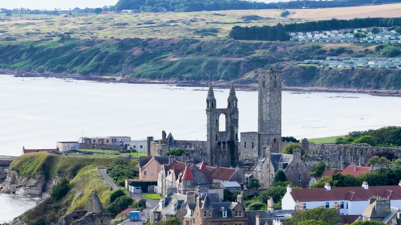 Drone shot reveals historic cathedral ruins, coastal cliffs, and town rooftops in bright daylight