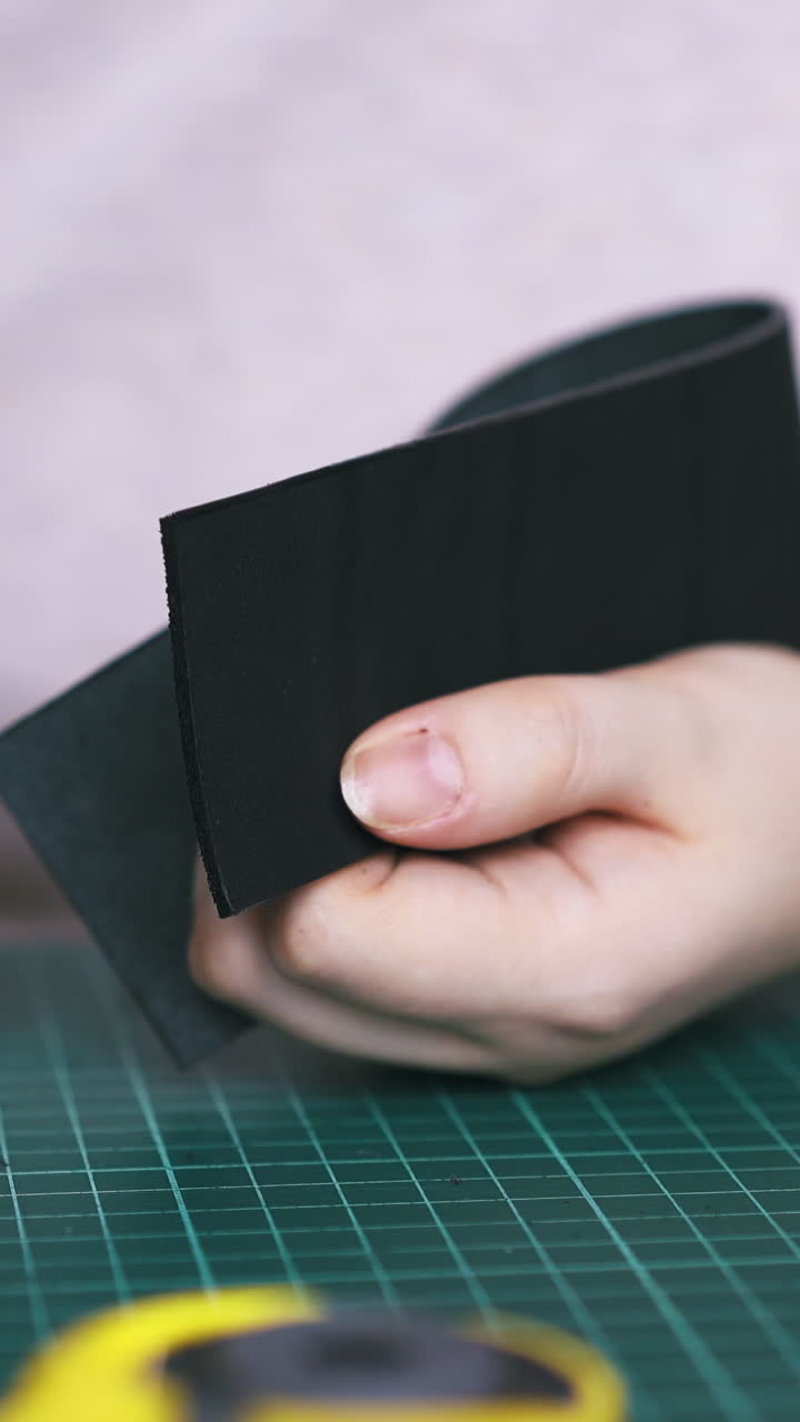 CU: Skilled tailor colours black leather strip edges with special oil pen and paint in workshop extreme close view