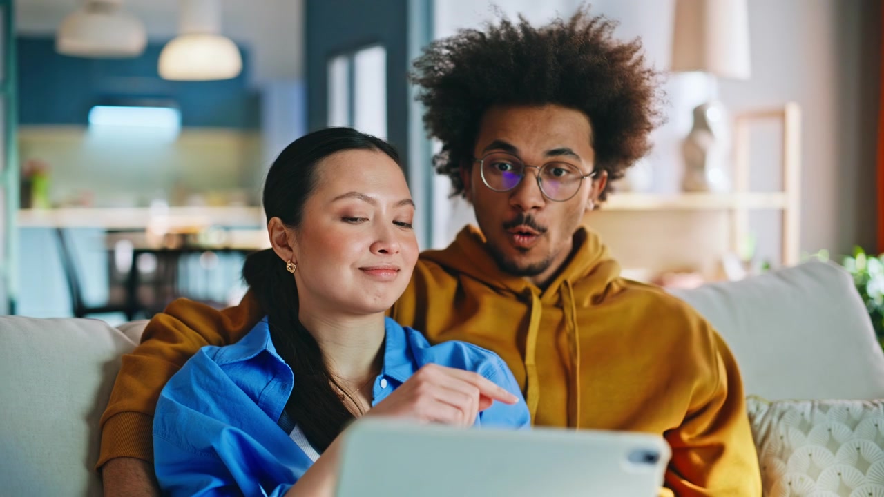 Multiethnic couple browsing tablet sofa. Pair shopping online together at home.