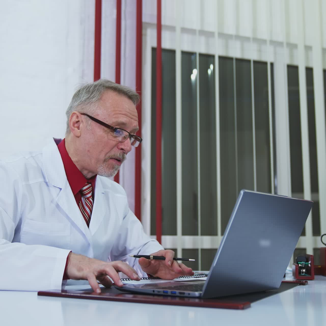 Online consultation in health service. Medical specialist giving a training talk in front of laptop gesticulating a lot. Senior doctor explains treatment to a patient during distant meeting.