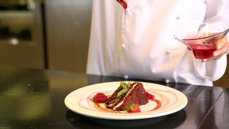 chef pouring strawberry sauce over chocolate cake