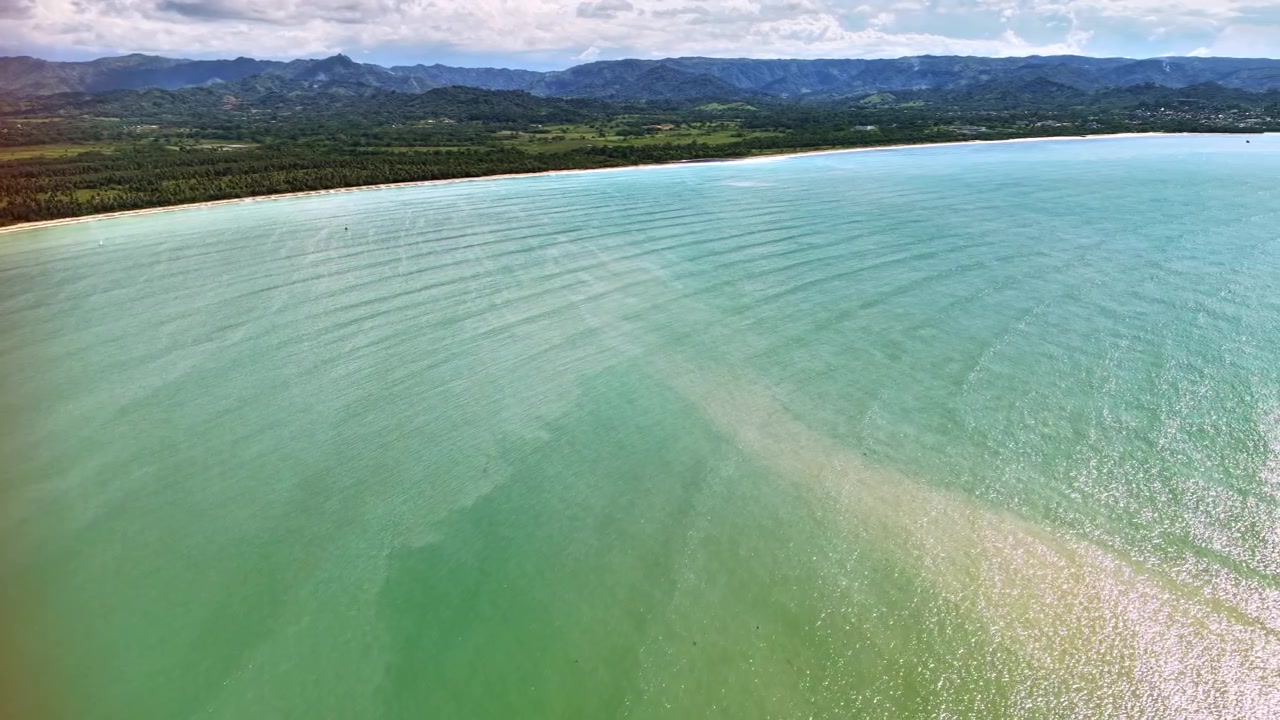 ドミニカ共和国サマナの、後ろに緑の山々がそびえ、砂浜に沿って穏やかな水面が広がる広大な湾の高高度ドローン空撮