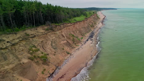 Aerial-drone-forward-moving-shot-over-wavy-ocean-along-dense-forest-with-green-trees-under-cloudy-day