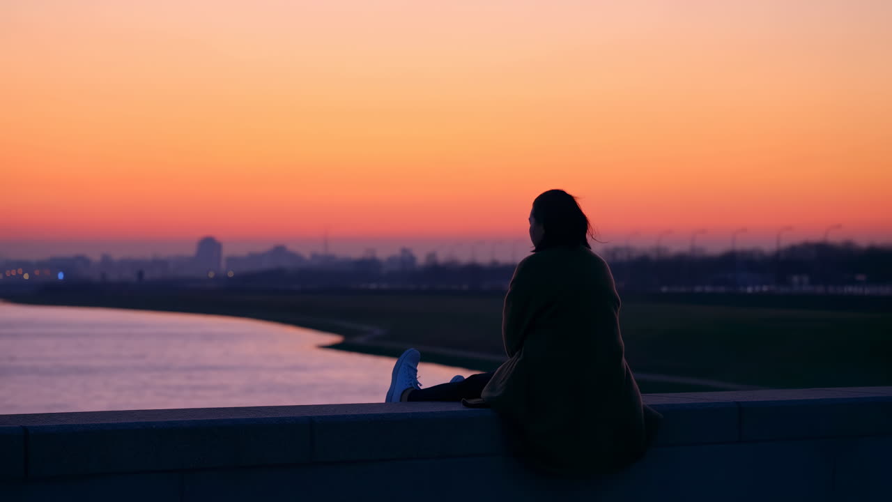 Donna seduta in silhouette che guarda il tramonto sulla città.