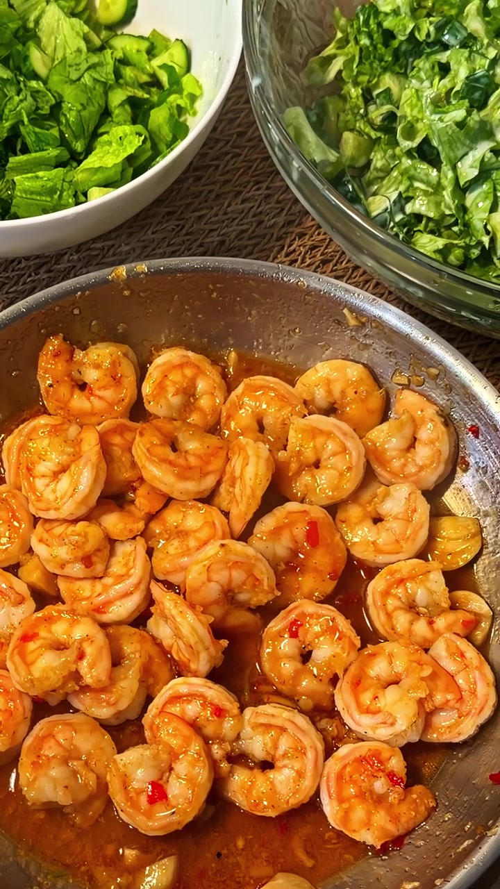 Camarão salteado com alho acompanhado de pratos como saladas verdes. Plano vertical, com zoom.