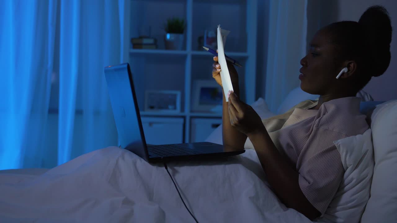 Premium stock video - African woman with laptop working in bed at night ...