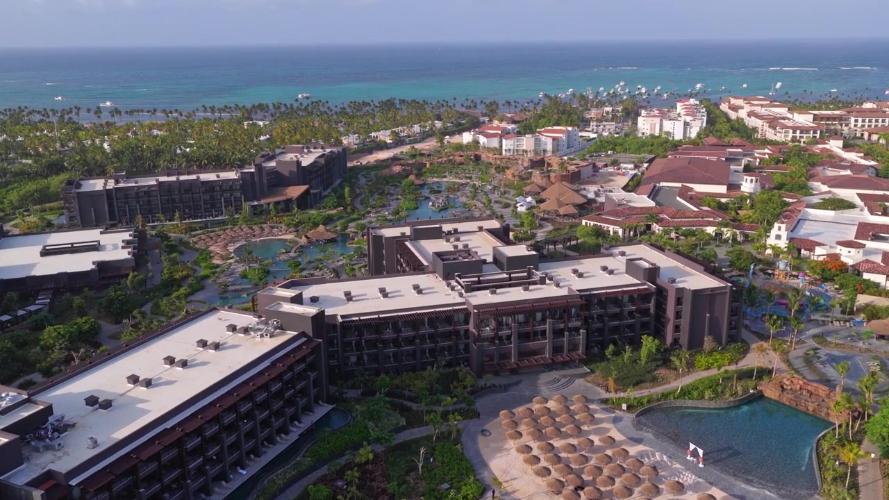 Drone in volo in avanti sopra un lussuoso resort tropicale con piscine, attrazioni acquatiche, palme e il Mar dei Caraibi turchese a Punta Cana.