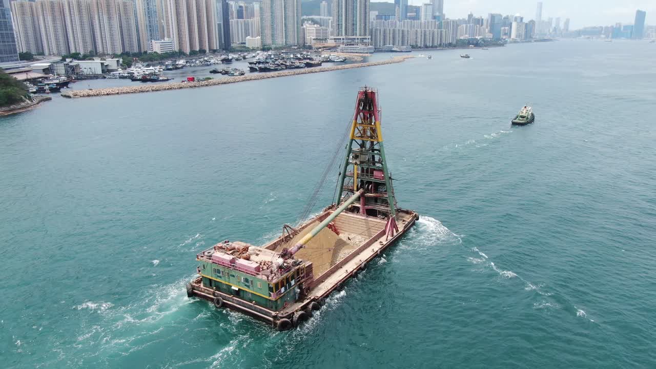Tugboat pulling a barge loaded with fresh excavated Sand along Hong Kong coastline, Aerial view