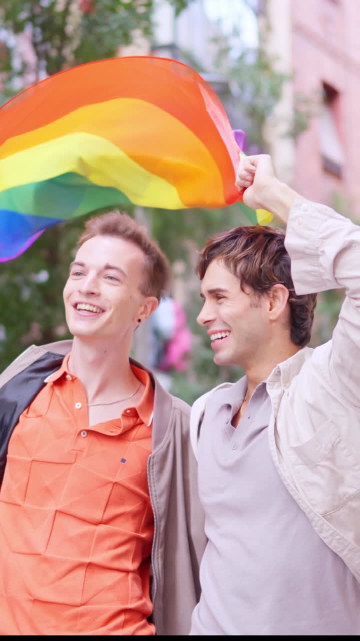 Happy Gay Couple Walking with Rainbow Flag on City Street